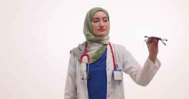 Tesettürlü Müslüman kadın doktor beyaz gözlük ve lens takıyor. Üniformalı kadın göz doktoru zayıf görüşlü hastaya çözümler sunuyor.