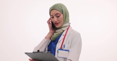 Tesettürlü kadın doktor telefon görüşmeleri yapıyor. Müslüman kadın hekim, akıllı telefon aracılığıyla online randevu veren tıbbi kayıtları dikkatle analiz eder.