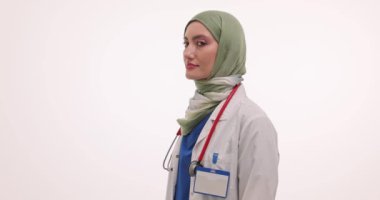 Müslüman kadın doktor gülümseyerek kollarını kavuşturuyor. Steteskoplu genç kadın doktor elleri göğsüne bağlı duruyor.