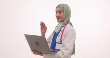 Müslüman kadın doktor video konferansında el sallıyor. Türbanlı genç kadın doktor bilgisayar kullanarak sanal danışmanlık yapıyor.