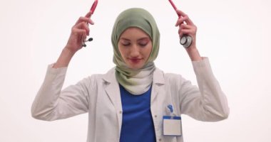 Müslüman kadın doktor gülümseyerek omuzlarına steteskop takıyor. Başörtülü kadın hekim randevusunda tıbbi aletle hastaları muayene etmeye hazırlanıyor