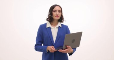 Genç iş kadını dizüstü bilgisayar tutuyor ve iyi bir jest yapıyor. Esmer kadın çalışan, kulaklıkla dizüstü bilgisayarında anlaşmanın yavaş çekim belirtilerini gösteriyor.