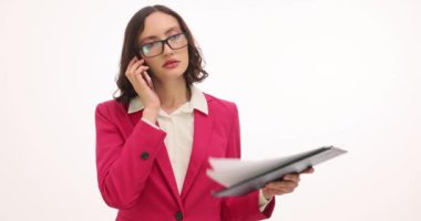 Gözlüklü esmer iş kadını cep telefonuyla konuşuyor. Kadın girişimci, telefon görüşmeleriyle ilgili belgeleri elinde tutuyor.