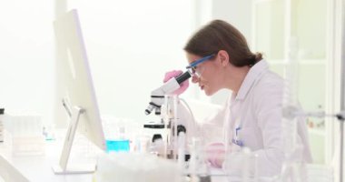 Bilimadamı mikroskoba bakıp test sonuçlarını dijital belgeye aktarıyor. Sıhhiye gelişmiş teknolojiyi gösteren dokunmatik ekran ile etkileşir