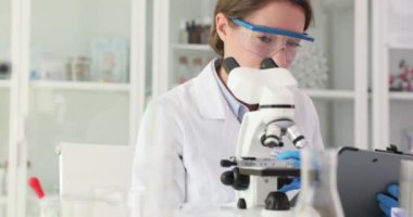 Kadın bilim adamı örnekleri mikroskop altında inceliyor. Üniformalı laboratuvar çalışanı modern ekipmanlarla araştırma yapıyor.