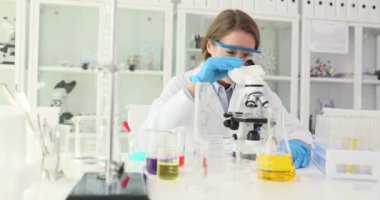Güvenlik gözlüklü kadın bilim adamı laboratuvarda mikroskopla çalışmayı bitirdi. Üniformalı gülümseyen kadın sonuçlardan memnun olduğunu ifade eder.