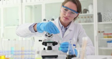 Kadın bilim adamı, Petri kabına pipetle birlikte ilaç bırakıyor. Laboratuvar çalışanı mikroskop altında inceleme için örnek hazırlar.