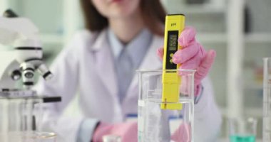 Bilimadamı laboratuvarda özel bir alet kullanarak sıvının pH 'ını ölçer. Üniformalı kadın laboratuvar çalışanı, asit oranını ölçer.