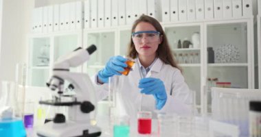 Üniformalı kadın bilim adamı deney tüpünden deney tüpüne kimyasal döküyor. Gözlüklü kadın laboratuvar çalışanı araştırma için numune hazırlıyor.