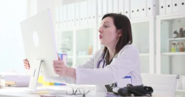 Kadın hekim bilgisayar ekranına bakar ve şaşırır. Profesyonel doktor masada oturur ve beklenmeyen test sonuçlarını yavaş çekimde analiz eder.