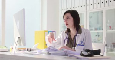 Yorgun kadın doktor, yığınla belgeyi analiz ediyor. Profesyonel esmer hekim yorgunluğu azaltmak için şakaklara masaj yapıyor.