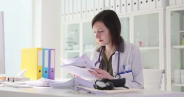 Konsantre kadın doktor tıbbi belgeleri analiz eder. Profesyonel doktor, ağır çekimden sonra hastaların laboratuvar sonuçlarını inceledi