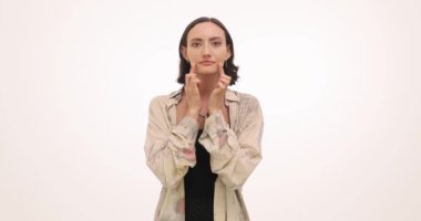 Üzgün suratlı bir kadın, beyaz arka planda parmakları olan dudakların köşelerini çeker. Esmer, gülümsemeyi taklit eder. Ağız köşelerini ağır çekimde çeker.