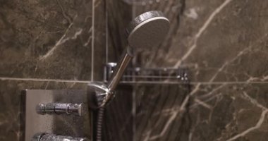 Kabinde mermer kiremitlerle duş başlığından su damlaları düşüyor. Modern banyo seti, krom detaylar ve dekore edilmiş duvarlar. İç mimari