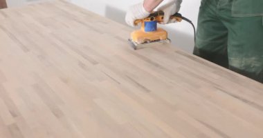 Eldivenli marangoz, kumdan masa başı ve elektrikli zımpara makinesi. Ahşap tozu, işçilik ve düz çevre atölyesindeki havayı dolduruyor.