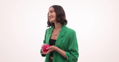 Yeşil elbiseli mutlu kadın beyaz arka planda kırmızı kalp oyuncağı tutuyor. Gülümseyen genç bayan, güzel hediyeler tutarak olumlu duygular ifade eder.