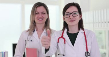 Kadın doktor, hastanede meslektaşının yanında baş parmak hareketi gösteriyor. Üniformalı kadın sağlıkçılar özel klinikte birlikte çalışıyorlar.