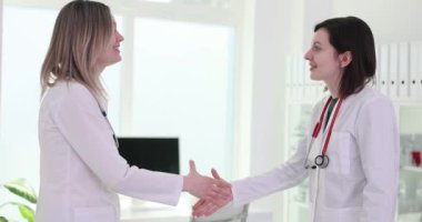 Üniformalı kadın doktorlar hastane ofisinde el sıkışıyor. Steteskoplu kadın sıhhiyeciler işbirliği için hazırlansın.
