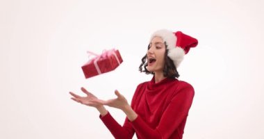 Noel Baba şapkalı mutlu kadın Noel hediyesini beyaz arka plana şakayla atıyor. Bayramlık kıyafetli bir kadın, mutluluğunu yavaş çekimle ifade eder.