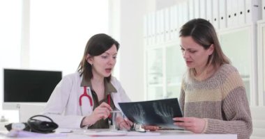 Kadın doktor masadaki kadın hastaya ayak röntgeni gösteriyor. Üniformalı doktor ağır çekimde travma ve tedavi seçeneklerini açıklıyor