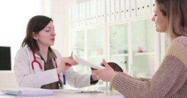 Kadın doktor kadın hastaya analiz sonuçlarını verir. Üniformalı doktor, başarılı bir tedaviyle sevinçten havalara uçtuğunu gösteriyor.