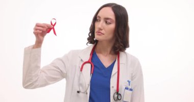 Kadın doktor beyaz arka planda kırmızı kurdele ve prezervatif gösteriyor. Üniformalı kadın doktor, hastanede AIDS 'li HIV hastalarına sağlık kampanyası düzenliyor