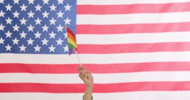 Canlı ve renkli bir gurur gösterisi. Amerikan bayrağının önünde gökkuşağı bayrağını gururla tutan bir el.