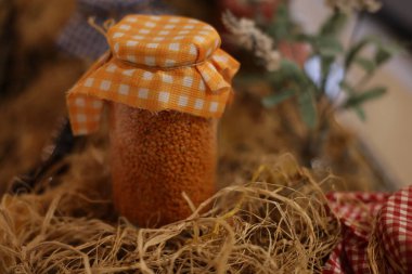 Parlak turuncu mercimeklerle dolu şık bir kavanoz, büyüleyici bir kareli kapakla süslenmiş, sonbahar temalı dekorasyon için mükemmel.