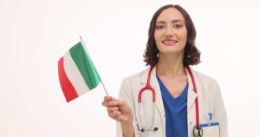 Cheerful young woman doctor waves small Italian flag. Female physician expresses excitement for international medical partnerships slow motion