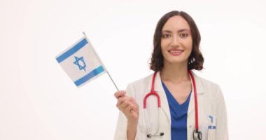 Genç kadın doktor beyaz arka planda İsrail bayrağı sallıyor. Tıbbi üniformalı kadın hekim, uluslararası hastaları işbirliği için karşıladı