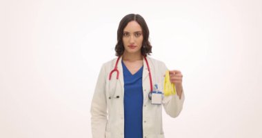 Kadın doktor bardağı şekerli ve mezuralı tutuyor. Üniformalı kadın doktor, şekerlerin kilo alma üzerindeki olumsuz etkisini vurguluyor