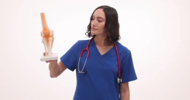 Kadın doktor diz eklemi modelini ve su toplamasını gösteriyor. Kadın hekim randevusunda hastanın eklem ağrısı için tedavi sunar