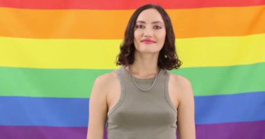 Mutlu genç kadın gökkuşağı bayrağına başparmak işareti yapıyor. Neşeli esmer kadın, neşeli gülüşü LGBT topluluğuna destek veriyor.
