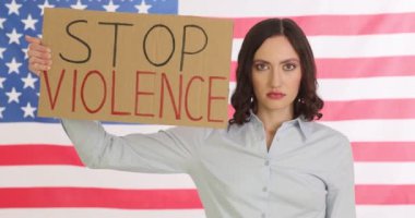 Kadın, Amerikan bayrağına yumruk sallayarak şiddeti durdurun işareti gösteriyor. Ciddi yüz ifadesi olan genç bir kadın aile içi şiddet hakkında hayati bir mesaj veriyor.
