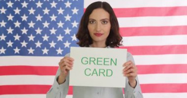 Mutlu kadının elinde Amerikan bayrağına karşı yeşil kart ifadesi var. Gülümseyen kadın, ABD 'de yaşama fırsatından duyduğu memnuniyeti dile getiriyor.
