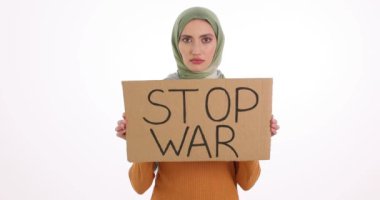 Türbanlı Müslüman kadın beyaz arka planda Savaş Durdurma işareti gösteriyor. Ciddi yüz ifadesi olan bir kadın, barış için yavaş çekimde protesto ediyor.