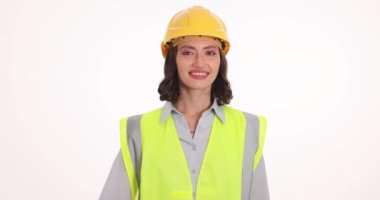 Miğferli kadın inşaat işçisi beyaz arka planda iyi bir hareket gösteriyor. Güvenlik üniforması içinde gülümseyen genç kadın, anlaşmanın ağır çekimde olduğunu gösteriyor.