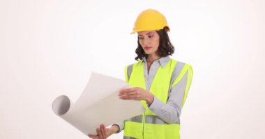 Güvenlik üniformalı kadın mimar beyaz arka plandaki kağıt planları açıyor. Miğferde odaklanmış genç bir kadın bina projesini inceliyor.