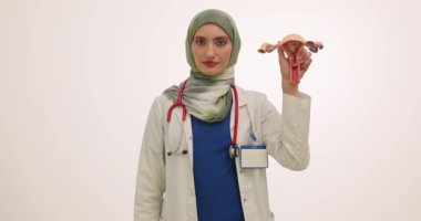 Başörtüsü içinde ciddi bir kadın doktor ilaç şişliği ve rahim mankeni tutuyor. Müslüman kadın uzman üreme sorunu tedavisi için yavaş çekimde uyuşturucu gösteriyor