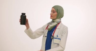 Türbanlı kadın doktor şişeden çok renkli vitamin kapsülleri dolduruyor. Müslüman kadın ilaçları belli bir yerde yavaş çekimde tutması gerektiğini gösteriyor.