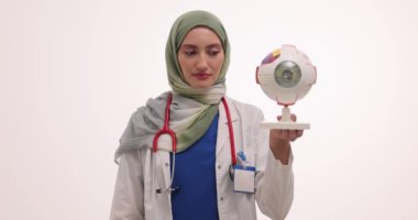 Müslüman kadın doktor kapsülleri su topladı ve göz yapısı modelini elinde tutuyor. Kadın tesettür uzmanı görme yeteneğini yavaş çekimde tutmak için araçları gösterir