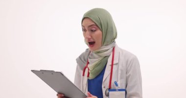 Tesettürlü gülümseyen kadın doktor elinde dosyayla mutlu bir şekilde çığlık atıyor. Müslüman kadın uzman, olumlu bilgileri ağır çekimde içeren belgeleri okuyor