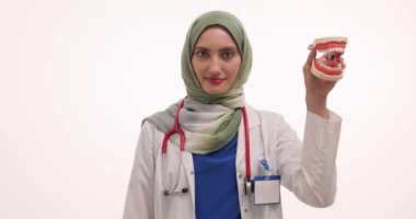 Steteskoplu kadın diş fırçası ve çene modeli gösteriyor. Gülümseyen genç doktor oral hijyen için farklı diş teçhizatı gösteriyor.