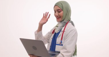 Başörtülü Müslüman kadın doktor, online randevusunda hastayla dizüstü bilgisayarla iletişim kuruyor. Üniformalı işçiler bilgisayar ekranına bakıyorlar.