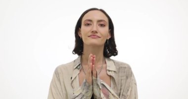 Neşeli genç bayan, beyaz arka plandaki ilgiye minnet göstermek için avuç içlerini birleştirir. Esmer kadın ağır çekimde tatmin olduğunu ifade ediyor.