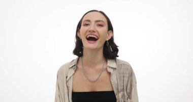 Yüzünde olumlu ifade olan genç bir kadın beyaz arka planda güler. Çekici esmer kadın günlük kıyafetlerle komik şakalardan hoşlanıyor ağır çekimde