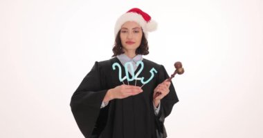 Noel Baba şapkalı kadın yargıç gelecek yılın 2025 hanesini yükseltti. Siyah cüppeli kadın yargıç beyaz arka planda bayram sezonunu kutluyor.
