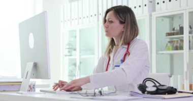 Bilgisayar klavyesinde sinirli kadın doktor tipleri ve hastane ofisinde notlar. Sarışın kadın terapist gergin bir şekilde masada oturuyor.