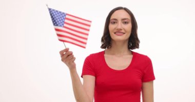 Gülümseyen kadın beyaz arka planda ülkeye destek veren Amerikan bayrağını sallıyor. Kadın ulusal sembolü kullanarak vatansever duygular taşıyor.