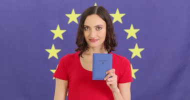 Gülümseyen kadın pasaport tutuyor ve arka planında Avrupa Birliği bayrağı olan olumlu bir jest gösteriyor. Kadın, mutluluk saçan bir pasaport gösteriyor